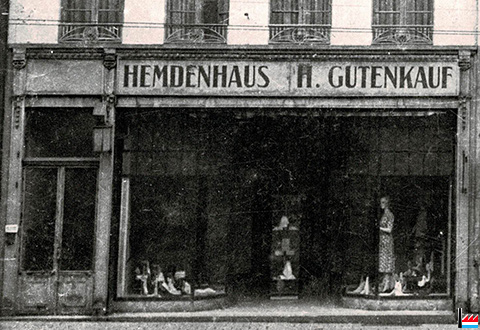 Old image of a storefront with "Hemdenhaus H. Gutenkauf" as the store name, from around the 1800s. The image shows the storefront with a display of shoes and a woman's mannequin in a dress.